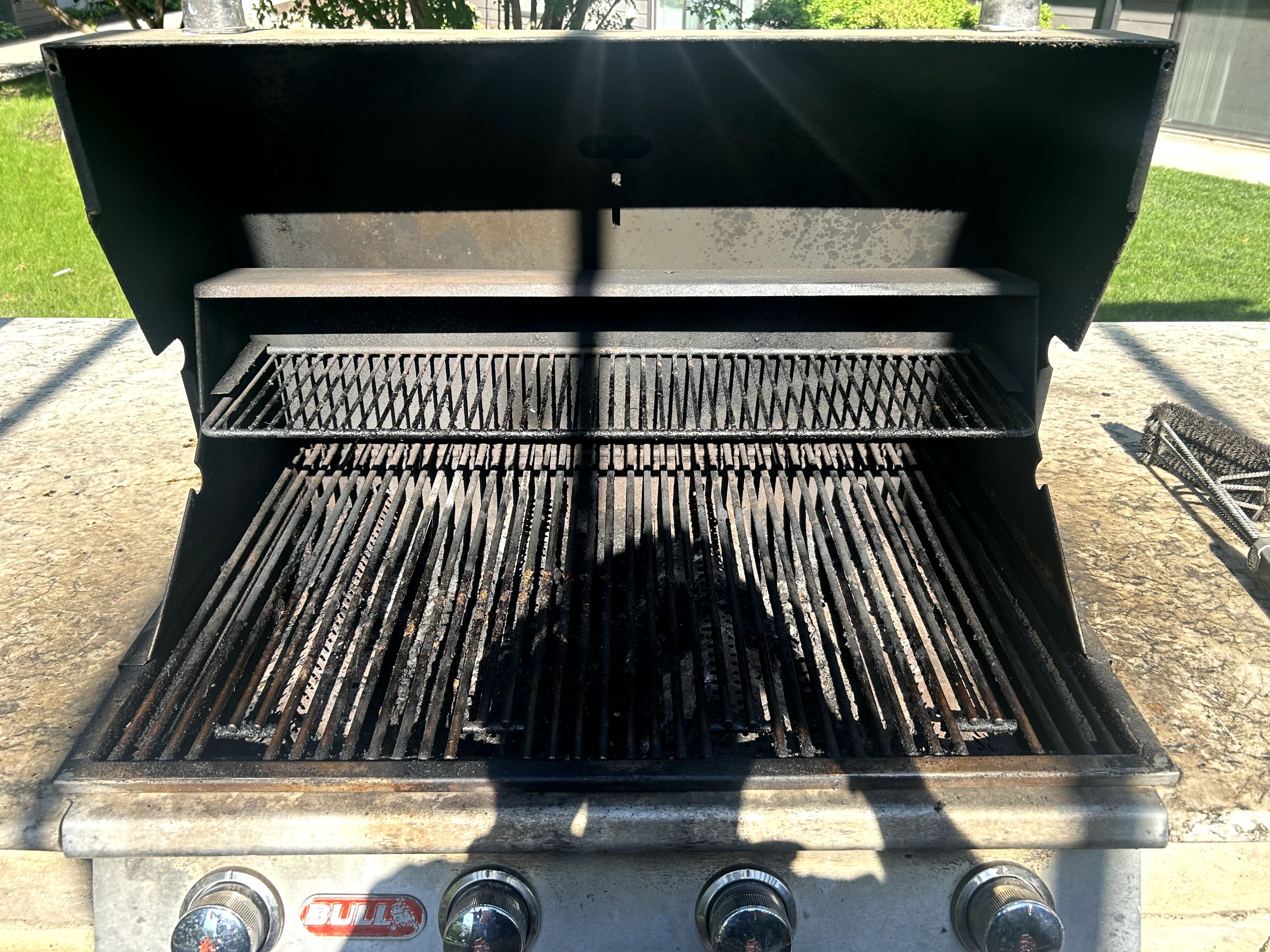 Built-in BULL grill with main grates covered in heavy crusty carbon; warming rack soiled